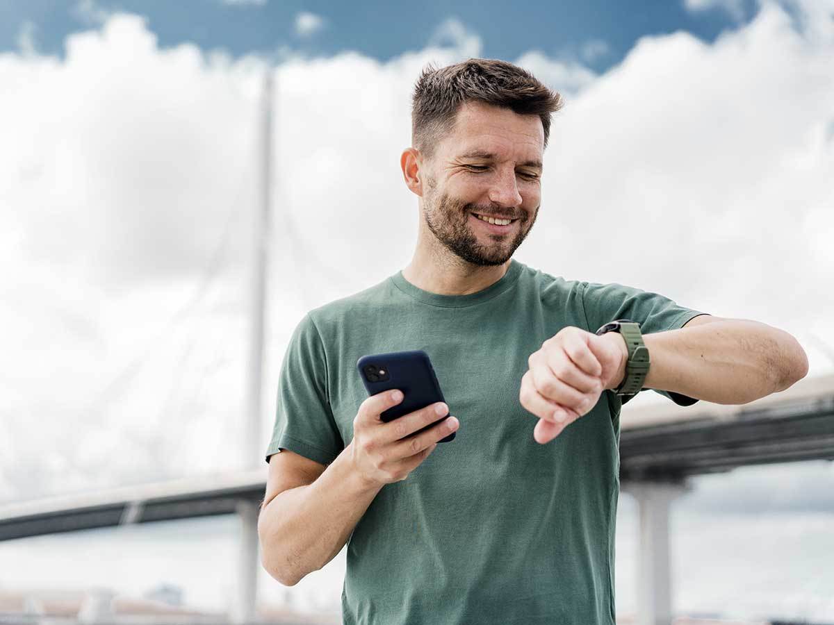 Čovek na treningu gleda u pametni sat i drži telefon Čovek na treningu gleda u pametni sat i drži telefon