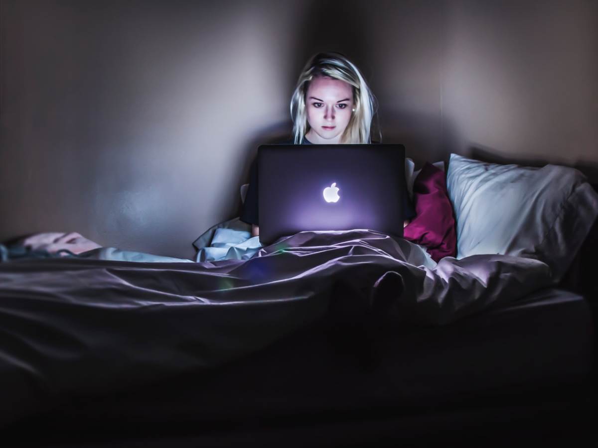  Devojka u krevetu radi nešto na Apple laptopu 