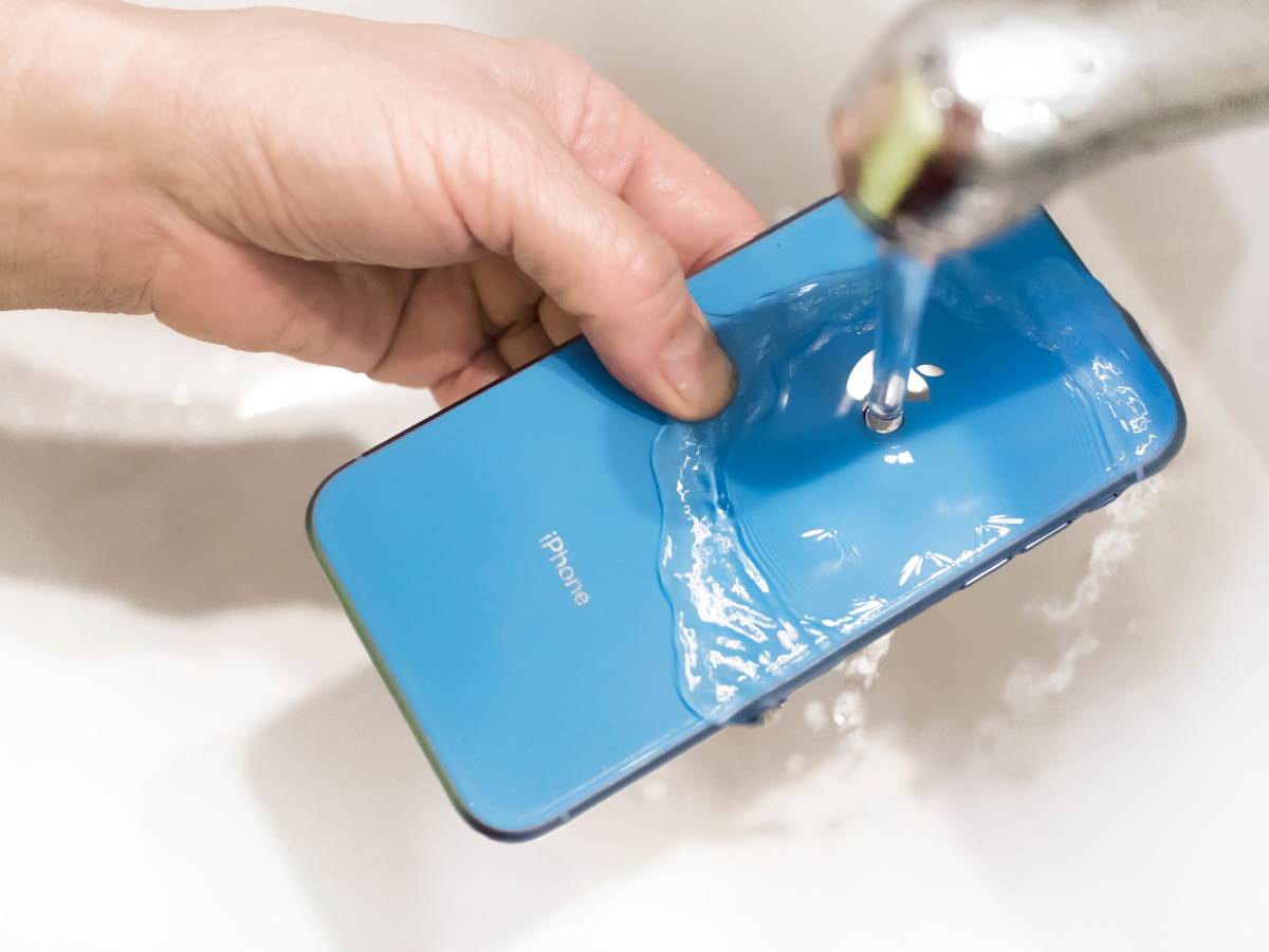 Čovek drži telefon ispod mlaza vode   Čovek drži telefon ispod mlaza vode