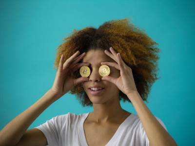 Devojka drži dva Bitcoin novčića na očima 